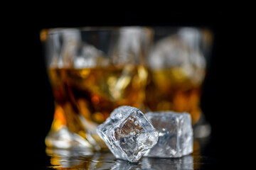 Glass of whiskey with cube ice on black background