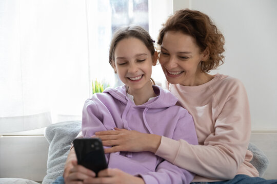 Smiling young mother and teenage daughter make self-portrait picture on smartphone together, happy mom and teen girl have fun using playing on cellphone gadget at home, technology concept