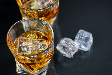 Glass of whiskey with cube ice on black background