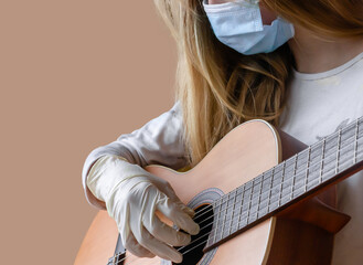A Girl with medical face mask and medical gloves playing acoustic guitar during the coronavirus...