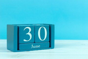 wooden calendar with the date of June 30 on a blue wooden background