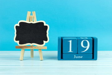 wooden calendar with the date of June 19 and an easel on a blue background, place for text, World Sickle Cell Anemia Awareness Day, World Walking Day, World Children's Football Day