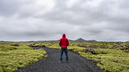 Man hiking in Iceland with backpack looking at the beautiful view of mountains surrounded by volcanic rocks and green moss near the Blue Lagoon in Reykjanes Peninsula