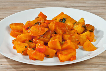 Potatoes in a white plate on a wooden table. Boiled potatoes with orange sauce.