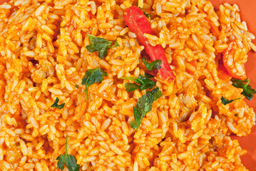 Pilaf with meat, cucumbers, greens and carrots in an orange plate.