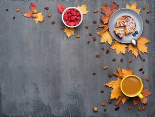 Seasonal autumn background. Frame of colorful maple leaves and a cup of hot drink, coffee, latte or cappuccino, nutmeg, cake, raspberries and cinnamon over grey.