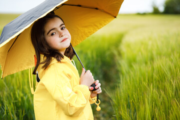 Pretty brunette girl standing in a field with an umbrella in her hands