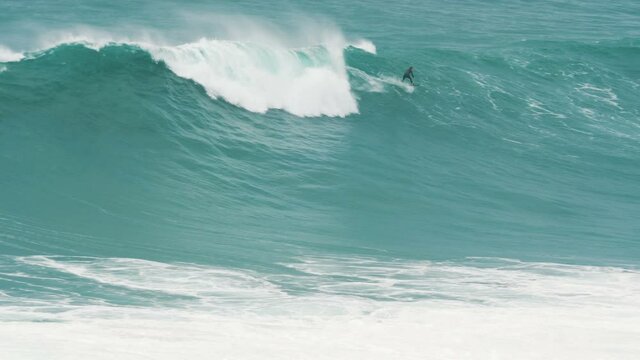 Surfer rides giant blue ocean wave. Big wave surfing in Portugal, Nazare. Slow motion