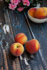 peaches on a dark wooden background, blurred flowers in the background and a plate of peaches