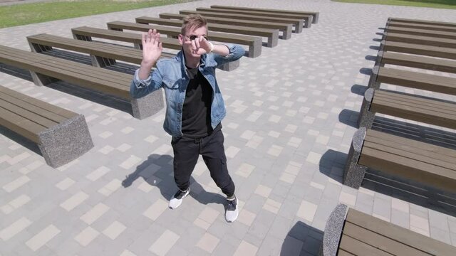 The guy making dance moves and poses, practicing in break dance in park between rows of benches. Hip hop culture. Repetition. Contemporary. Slow motion