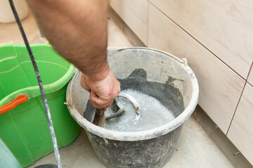 The worker cleans the propeller from an electric mixer with a cement adhesive for ceramic tiles in a bucket full of water.