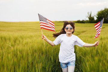 Pretty young pre-teen girl in field holding American flag.