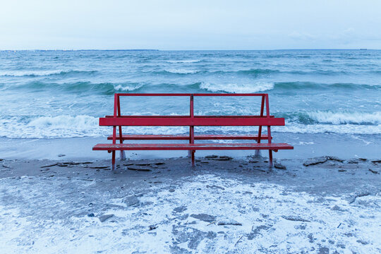 Red bench covered by ice is hit by winter sea. Icy waves of Baltic sea on empty beach. © yegorov_nick