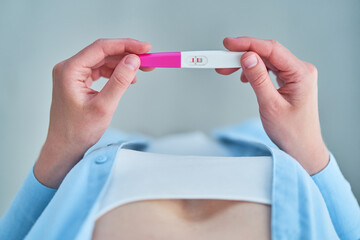 Woman hopes to get pregnant and holds in hands a pregnancy test with two stripes. Top view