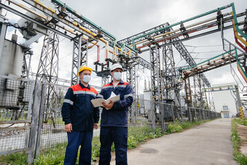 Engineers electrical substations conduct a survey of modern high-voltage equipment in the mask at the time of pandemia. Energy. Industry