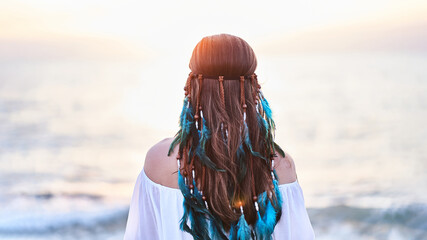 Serene peaceful tranquil boho hippie woman with blue feathers in hair standing back and looking to sea. Calm and freedom concept © Goffkein