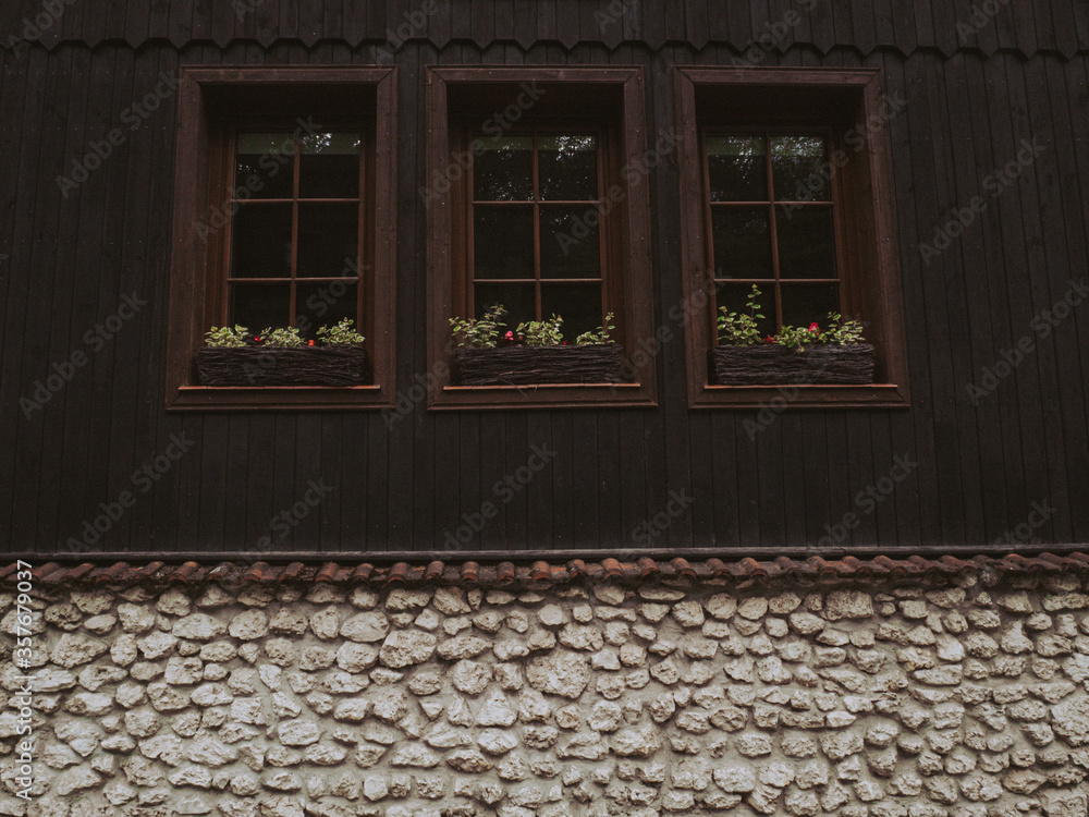 Wall mural fragment of a wall of an old brown wooden house with three windows and a stone basement.