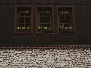 Fragment of a wall of an old brown wooden house with three windows and a stone basement.
