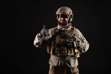 USA soldier in a military suit with a rifle smiles and shows a like against a dark background, an American commando in uniform