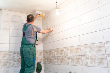 A construction worker applies leveling compound to the ceiling with a stainless steel trowel. Works...