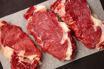 three steaks of raw marbled beef on parchment paper, top view