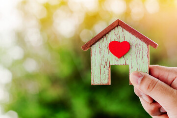 Hand holding a wooden house model in bokeh tree background, Financial planning to buy a first home for the family concept.