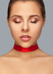 Beautiful woman with clean skin and pink makeup, with closed eyes with a red ribbon on her neck.  Makeup and cosmetology concept.