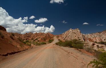 Travel. Empty Dirt road across the arid desert and red hills.