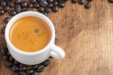 Aerial view of white cup with coffee on wooden table with coffee beans, horizontal, with copy space