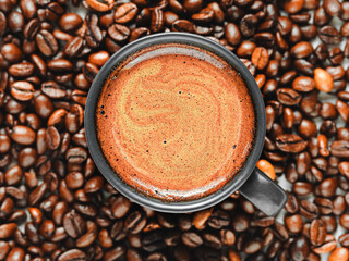 Espresso cup with froth among roasted coffee beans, flat lay, close-up. Strong aromatic coffee