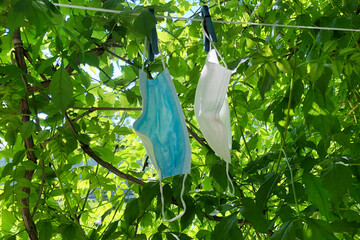 two medical protective masks hang on clothesline in green trees, drying on air. Obligatory wearing of protective masks due to new healthcare restrictions. Protection from viruses.
