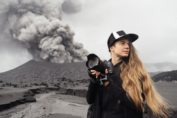 girl travel photographer stands with camera against the backdrop of an erupting volcano