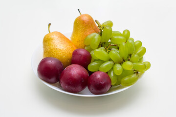 fruit in a plate on a white background, grapes, plums, pears, fruit diet
