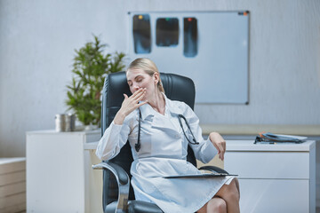 A medical worker at his Desk yawns with fatigue covering his mouth with his hand