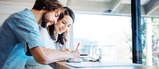 Naklejka premium Couple working together at home in bright wooden room in their own house. Remote workplace. Solving tasks at the desk. Wide screen panoramic