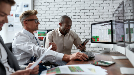 Learn Together. Successful businessmen trading stocks. Stock traders looking at graphs, indexes and numbers on multiple computer screens. Three colleagues in modern office