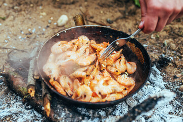 The cook stirs with a fork the sizzling shrimps that are fried in a pan in oil - seafood in a spicy garlic sauce