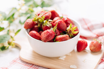 Fresh garden strawberry in a plate on a wooden board with a beautiful napkin and a serving and a sprig of jasmine inflorescences, wholesome food and vitamins. Close-up