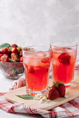 A refreshing summer drink made from strawberries, juice, soda with ice cubes and slices of berries, in a beautiful glass with water droplets, still life of cocktails on a wooden board, red napkin