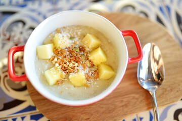 Pudding with fruits, nuts and seeds in red bowl on the table of cafe. Dessert. Healthy eating.