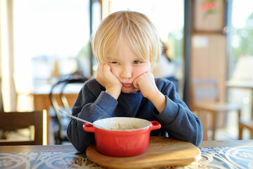 Little child sitting the table in cafe or restaurant and doesn't want to eat. Healthy food. Kids diet. Poor appetite.