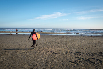 Fototapeta na wymiar Pacific Rim National Park Reserve, Canada, September 25, 2016 - A female surfer walks out to the ocean at one of Canada's top surf meccas, Long Beach, near the village of Tofino.
