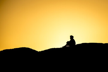 Silhouette of people sitting on large rock near Tofino, British Columbia, at sunset.