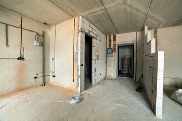 Interior of an apartment room with bare walls and ceiling under construction.