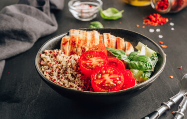 Healthy salad bowl with quinoa, tomatoes, chicken, cucumber and basil on black wooden background. Superfoods.