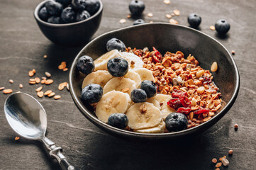 Healthy breakfast concept with homemade granola with banana and blueberries on black wooden background