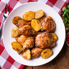 Chicken baked in pieces with potatoes and onion on a white dish.
