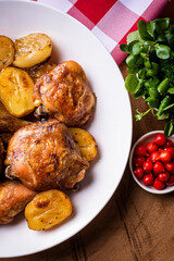 Chicken baked in pieces with potatoes and onion on a white dish.