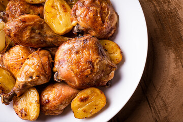 Chicken baked in pieces with potatoes and onion on a white dish.