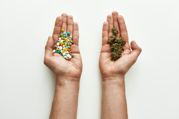 Top view of colorful pills in one hand and medical marijuana buds in another over white background. Concept of choice and herbal, alternative medicine